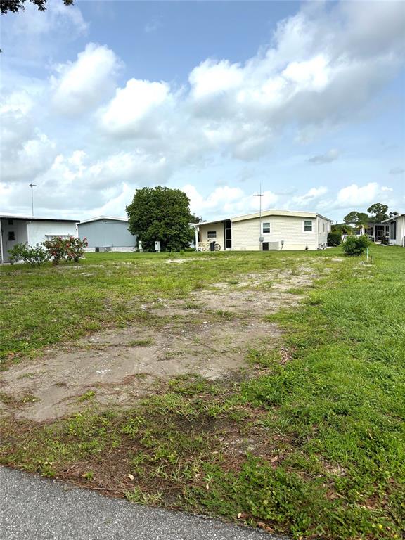 A vacant lot sits between two manufactured homes under a blue sky with scattered clouds — 236 EL PRADO, NORTH PORT, FL