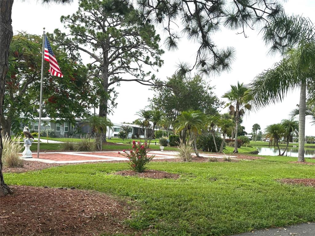A flag pole and a brick patio are situated on a lawn near a pond — 236 EL PRADO, NORTH PORT, FL
