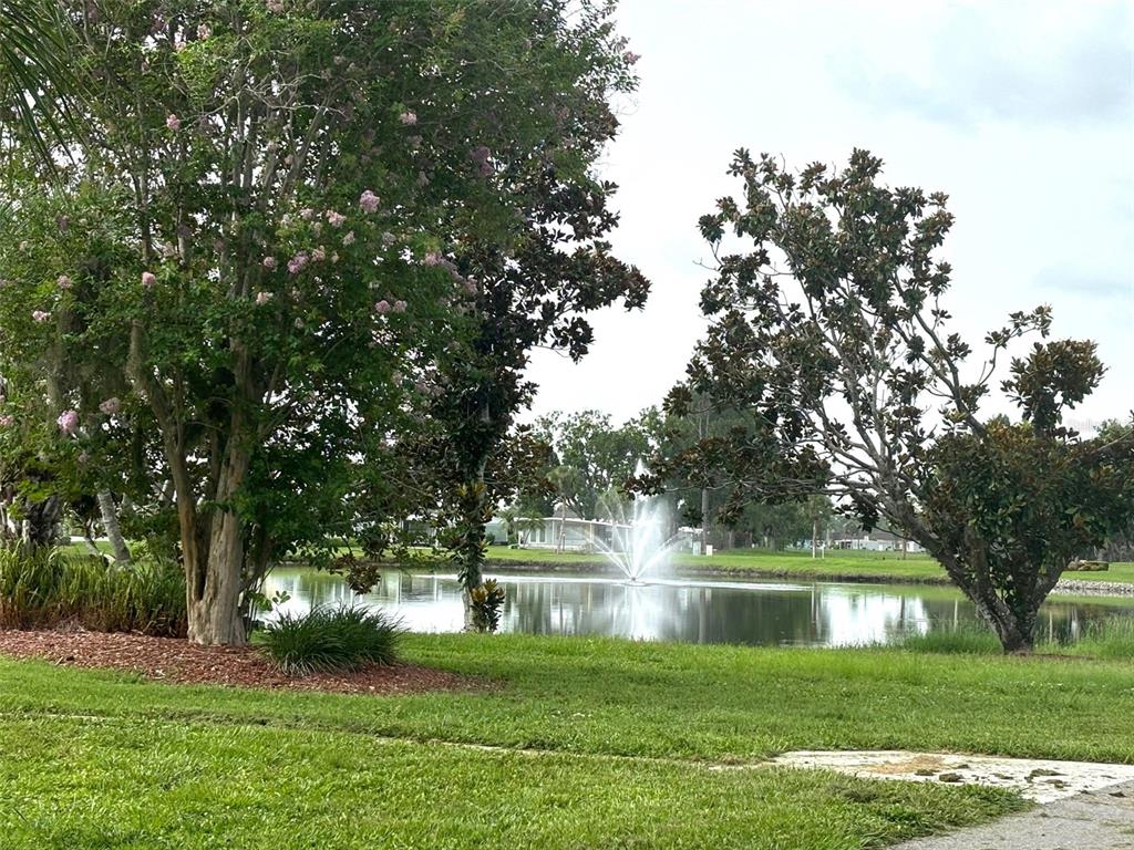 A pond with a fountain is surrounded by green grass and mature trees — 236 EL PRADO, NORTH PORT, FL