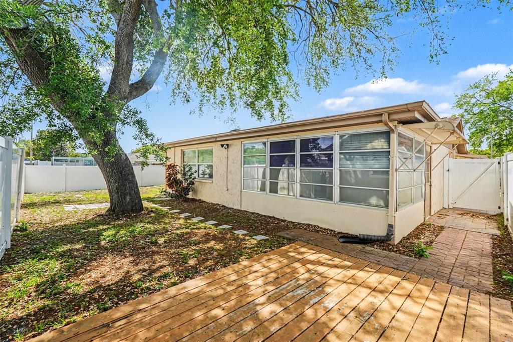 A backyard view showing a wooden deck, a tan house with a sunroom, and a tree — 7255 FIRESIDE DRIVE, PORT RICHEY, FL