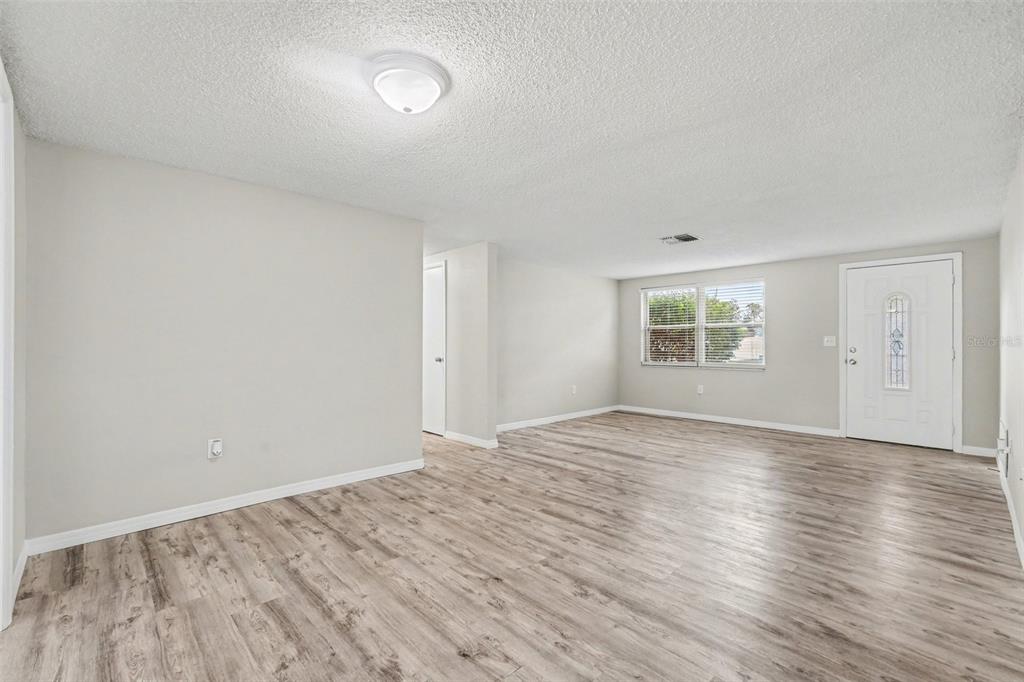 An empty living room with light gray walls, wood-look flooring, and a white front door — 7255 FIRESIDE DRIVE, PORT RICHEY, FL