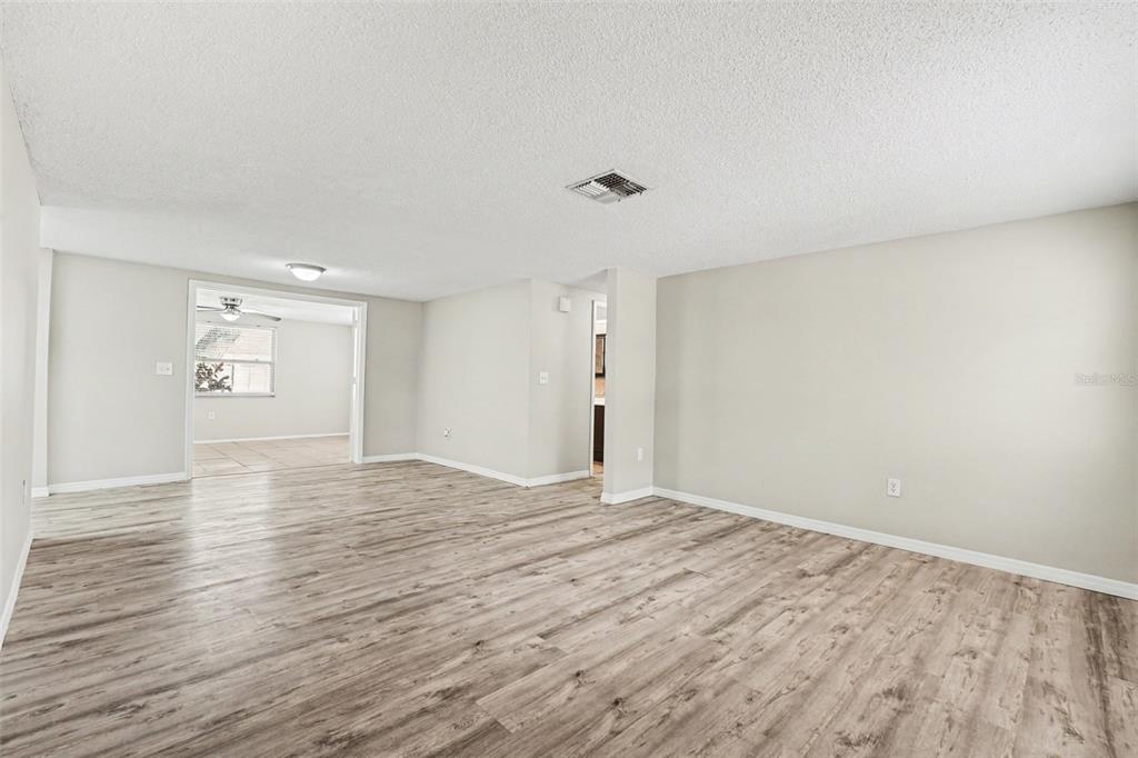 An empty room with light gray walls and wood-look flooring leads to an adjacent space — 7255 FIRESIDE DRIVE, PORT RICHEY, FL