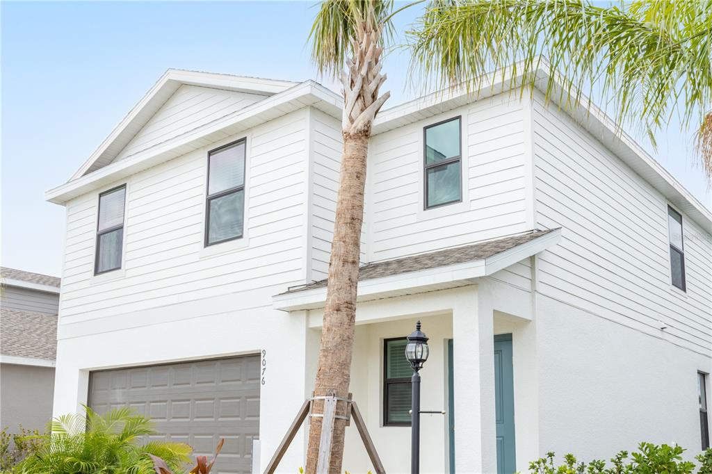 A two-story white house with horizontal siding, a gray garage door, and a palm tree — 9076 TEQUILA SUNRISE DRIVE, SARASOTA, FL