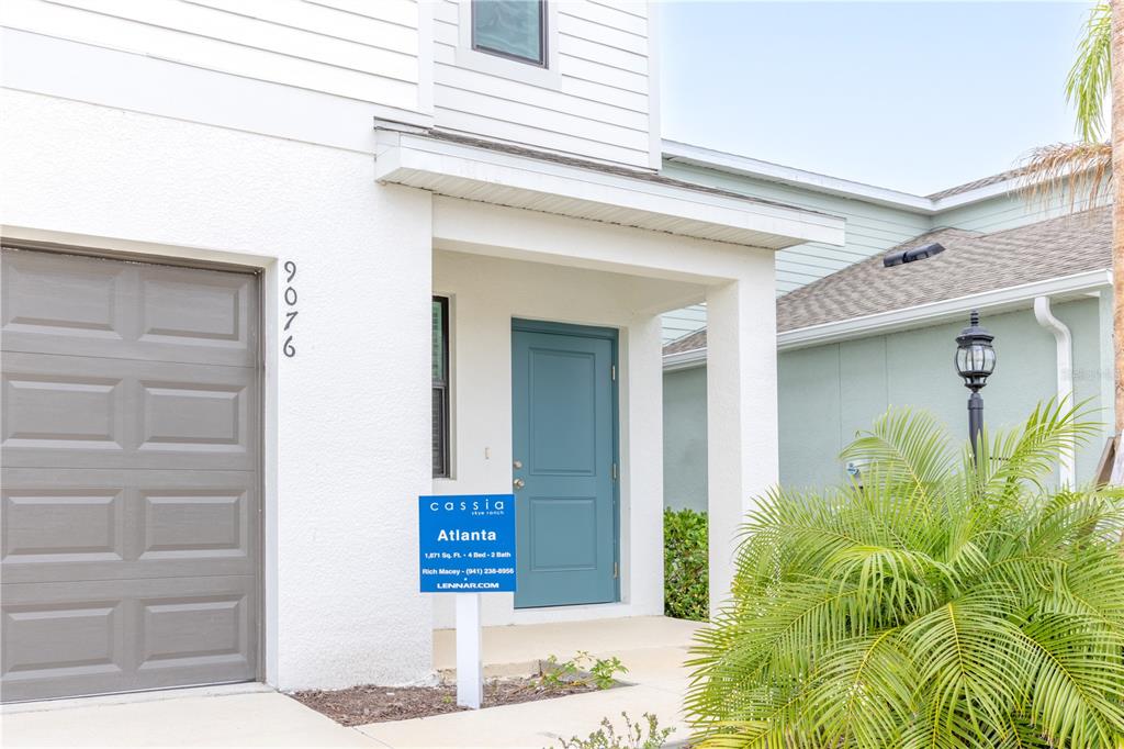 A white house exterior features a gray garage door, a blue front door, and landscaping — 9076 TEQUILA SUNRISE DRIVE, SARASOTA, FL