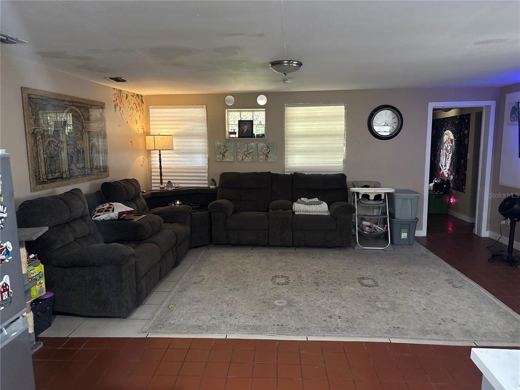 A living room features a brown sofa, a large area rug, and a wall-mounted television — 6115 CLIFF AVENUE, GIBSONTON, FL