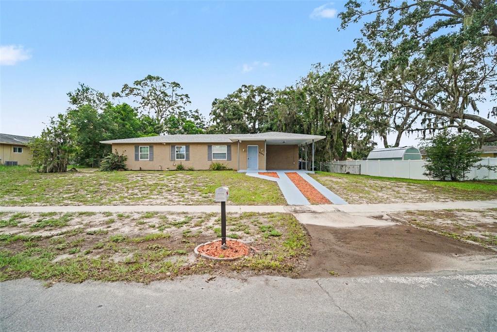 A single-story house with a tan exterior, a carport, and a front yard with sparse grass — 6925 TREEHAVEN DRIVE, SPRING HILL, FL