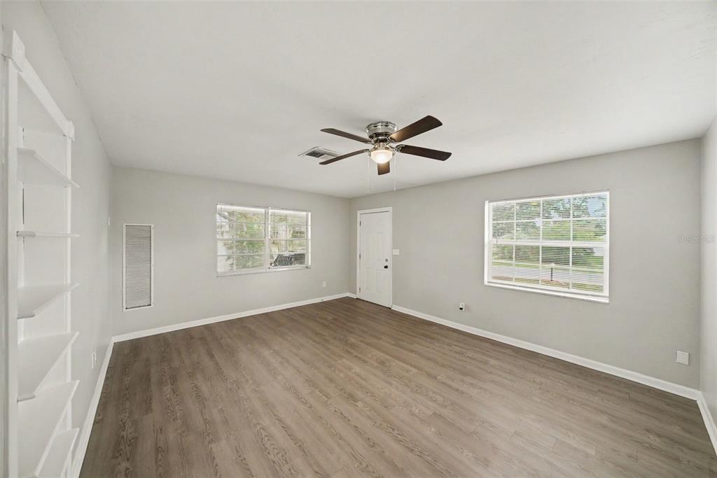 An empty room with light gray walls, wood-look flooring, a ceiling fan, and two windows — 6925 TREEHAVEN DRIVE, SPRING HILL, FL