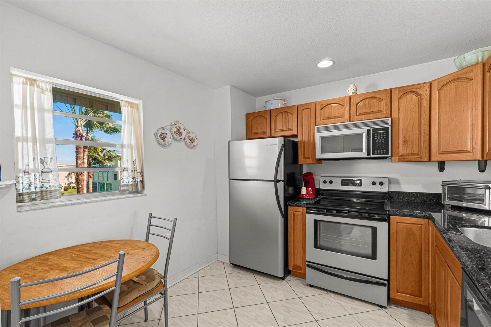 A kitchen features wood cabinets, stainless steel appliances, dark countertops, and a small dining area — 2515 NE 1st Court # 4100, Boynton Beach FL 33435, BOYNTON BEACH, FL