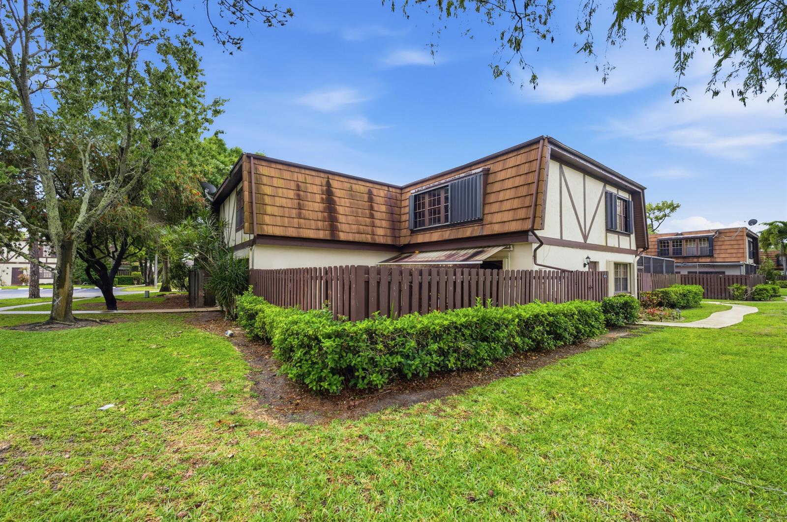 A two-story townhouse with brown shingled siding and a fenced yard sits on a lawn — 105 Weybridge Circle # A, Royal Palm Beach FL 33411, ROYAL PALM BEACH, FL