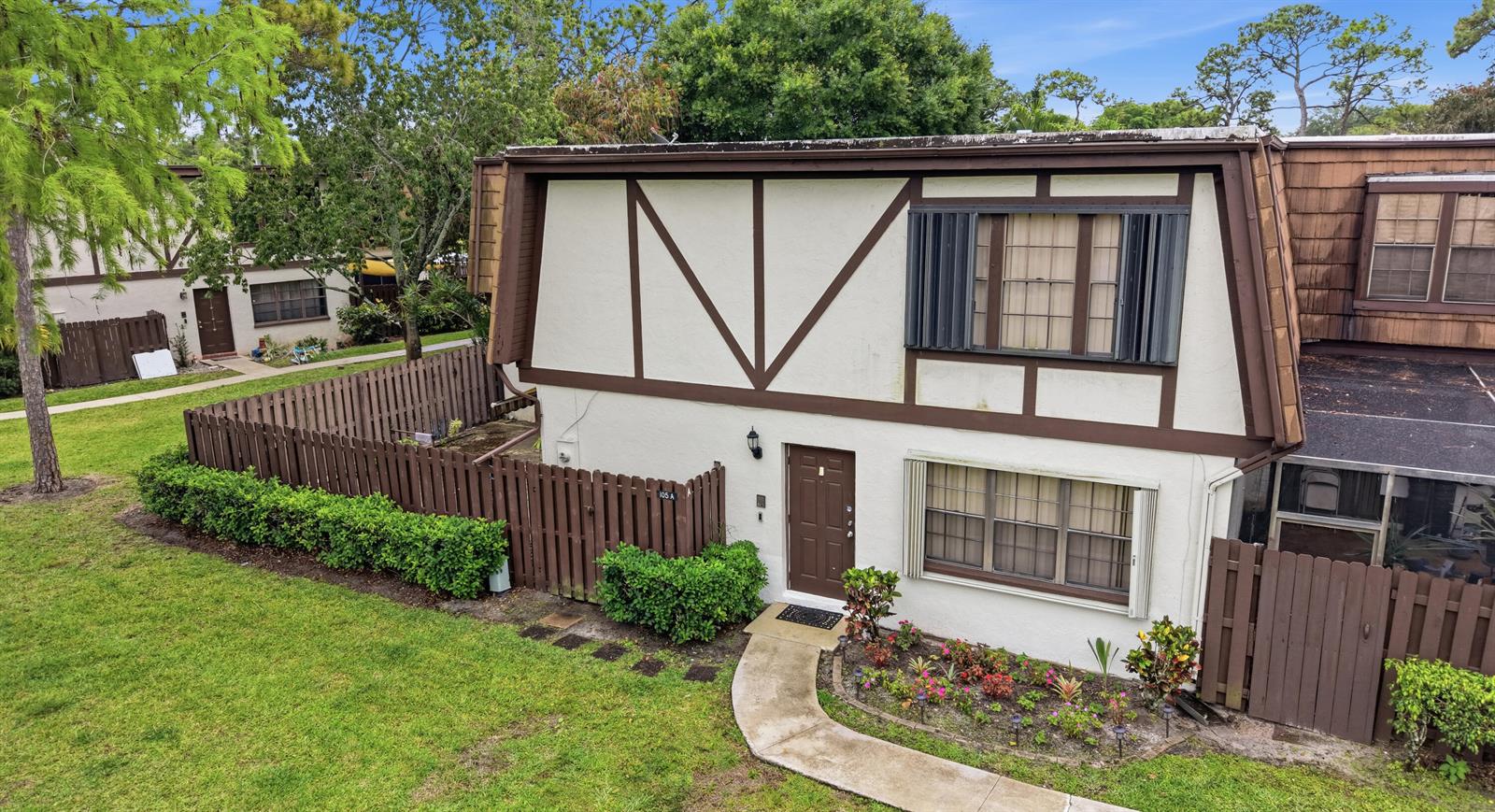 An exterior view of a two-story townhouse with a brown fence and a front garden — 105 Weybridge Circle # A, Royal Palm Beach FL 33411, ROYAL PALM BEACH, FL