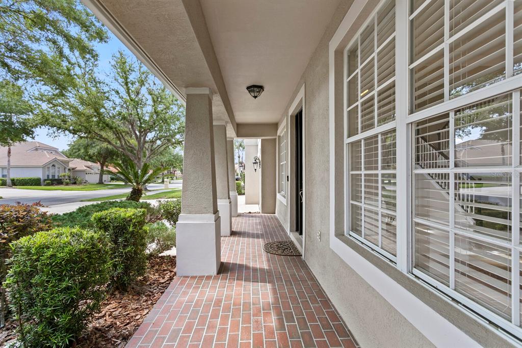 A covered front porch with brick flooring, columns, and a view of the neighborhood — 10235 ESTUARY DRIVE, TAMPA, FL