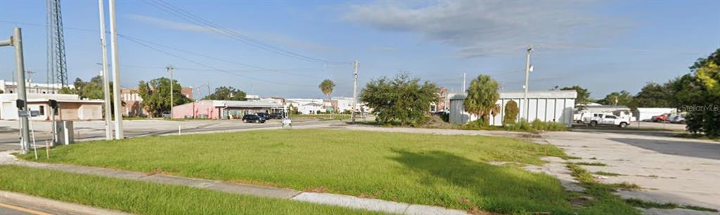 A vacant, grassy lot sits between paved areas and nearby commercial buildings under a blue sky — 103 N BREVARD AVENUE, ARCADIA, FL