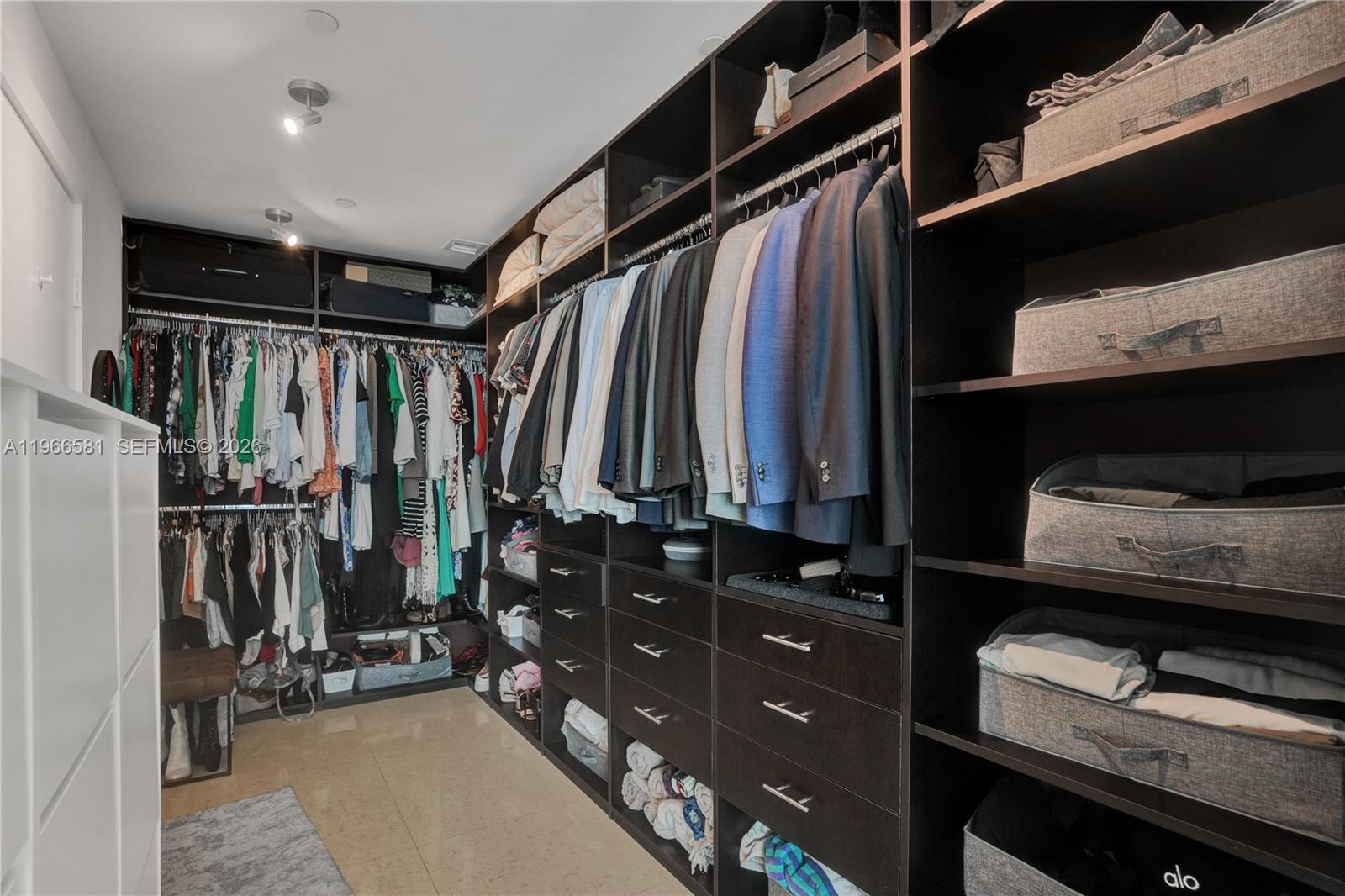 A walk-in closet features dark wood cabinetry, hanging clothes, and open shelving with storage bins — 900 Biscayne Blvd # 2907, Miami FL 33132, MIAMI, FL