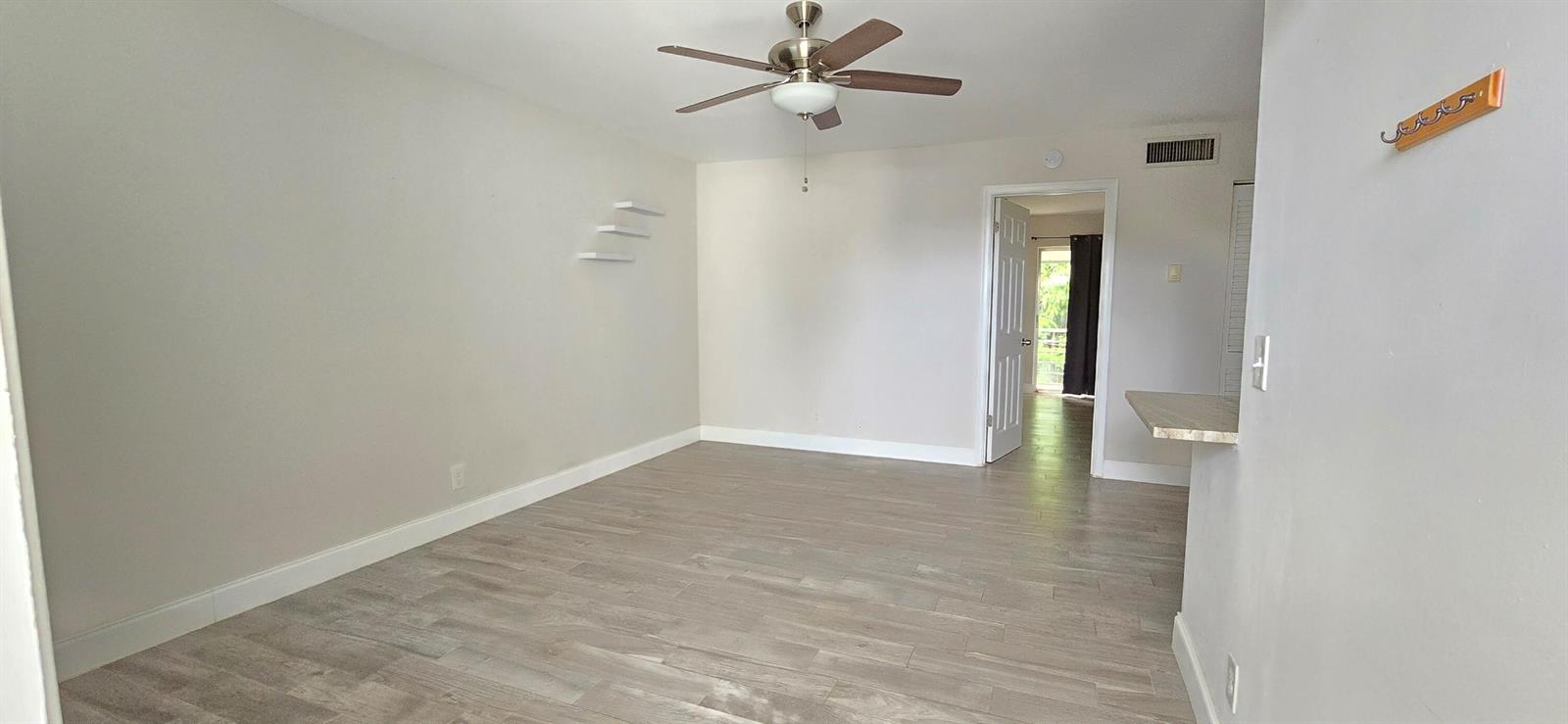 An empty living room features light wood-look flooring, a ceiling fan, and white walls — 115 SW 1st Avenue # 7, Boynton Beach FL 33435, BOYNTON BEACH, FL