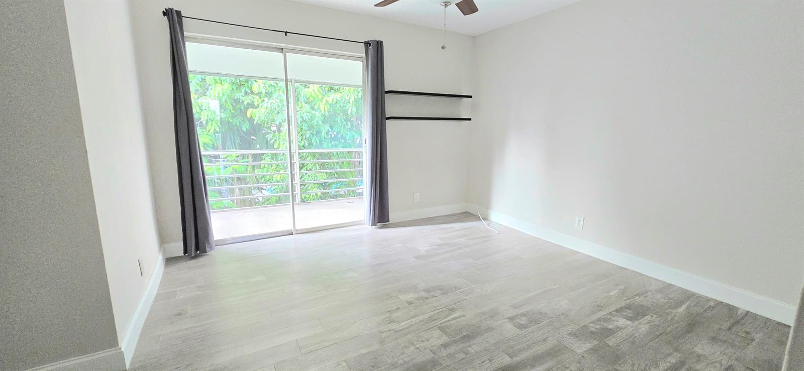 An empty room features light-colored wood-look tile flooring, gray curtains, and two wall-mounted shelves — 115 SW 1st Avenue # 7, Boynton Beach FL 33435, BOYNTON BEACH, FL