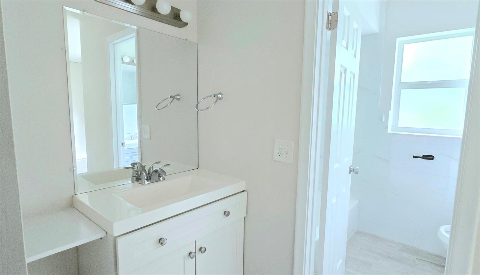 A bathroom features a white vanity with a sink, a mirror, and an adjacent shower — 115 SW 1st Avenue # 7, Boynton Beach FL 33435, BOYNTON BEACH, FL