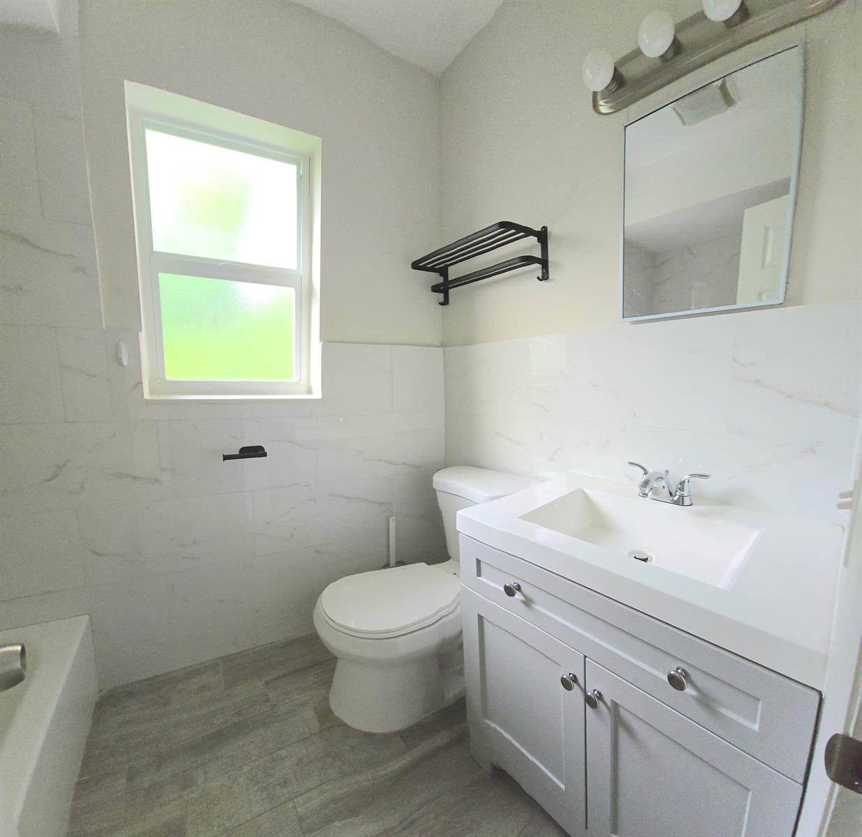 A bathroom features a white vanity, a toilet, a window, and marble-look wall tiles — 115 SW 1st Avenue # 7, Boynton Beach FL 33435, BOYNTON BEACH, FL