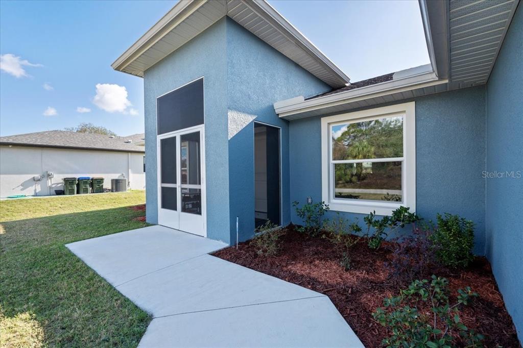 A blue stucco house exterior features a screened entryway, a concrete walkway, and landscaping — 2405 VANCOUVER LANE, NORTH PORT, FL