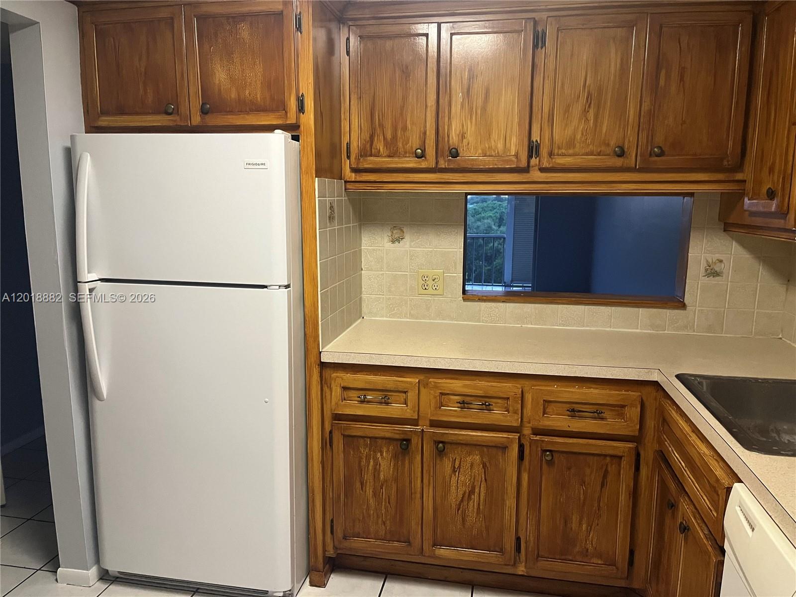 A kitchen features wood cabinets, a white refrigerator, a beige countertop, and a pass-through window — 950 Hillcrest Dr # 503, Hollywood FL 33021, HOLLYWOOD, FL