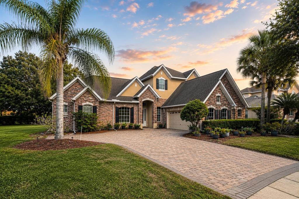 A brick and stucco house with a paver driveway and palm trees at sunset — 1724 BRIDGETS COURT, KISSIMMEE, FL