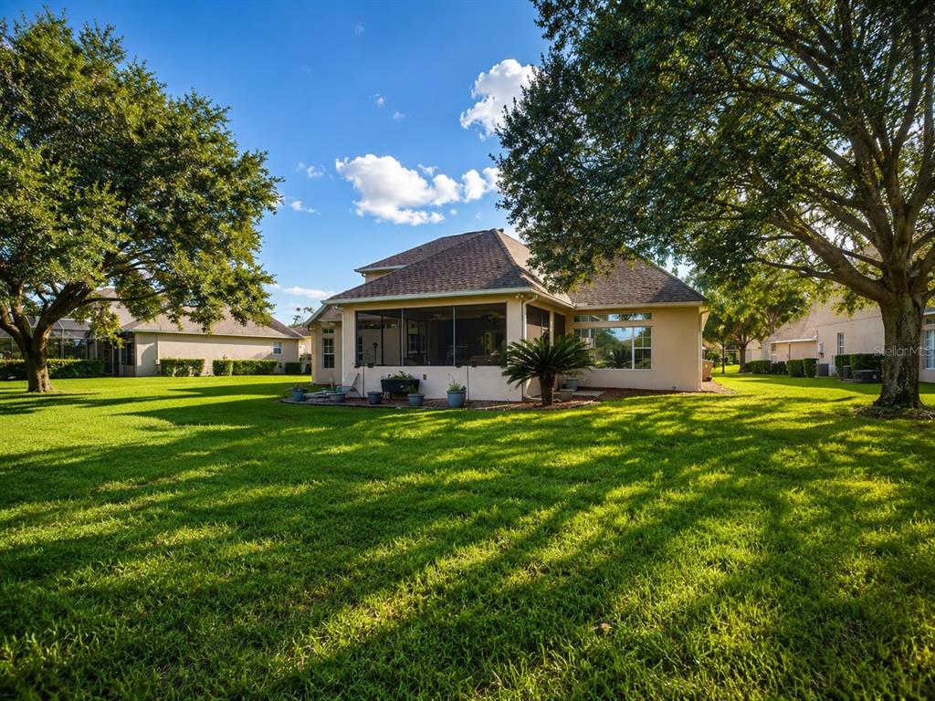 A view of the backyard and screened-in patio of a single-family home with large trees — 1724 BRIDGETS COURT, KISSIMMEE, FL