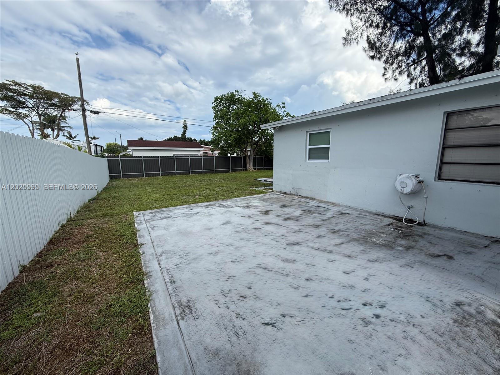 A concrete patio sits adjacent to a white house with a fenced backyard — 3900 SW 60th Ave, Davie FL 33314, DAVIE, FL