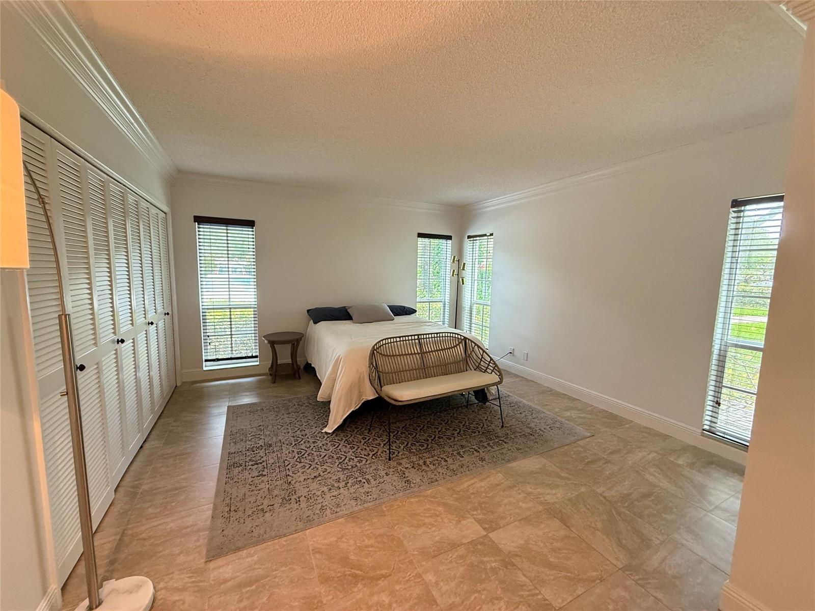 A bedroom with tile flooring, a bed, a bench, and white louvered closet doors — 3000 N Palm Aire Drive # 107, Pompano Beach FL 33069, POMPANO BEACH, FL