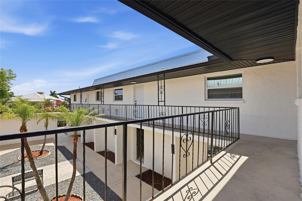 An elevated outdoor walkway with black metal railings overlooks a courtyard with palm trees — 4460 OAKLEY STREET, PUNTA GORDA, FL