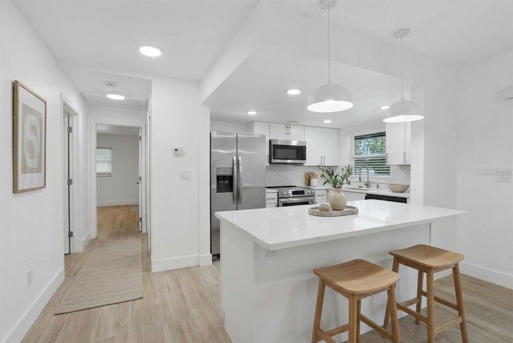 A modern white kitchen features a central island, stainless steel appliances, and light wood flooring — 4460 OAKLEY STREET, PUNTA GORDA, FL