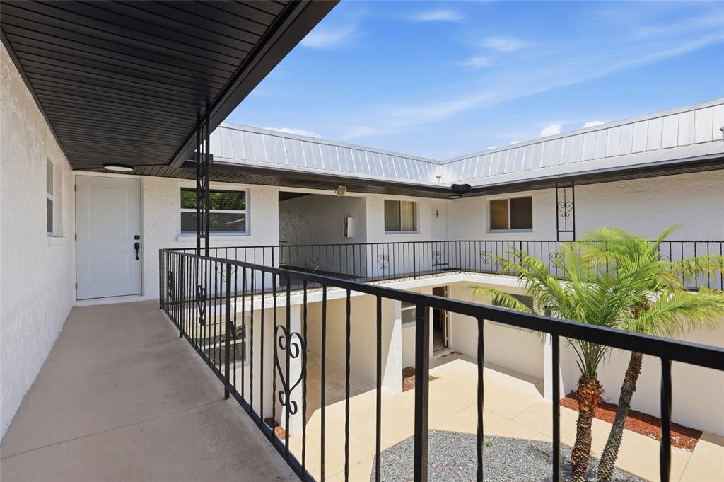 An elevated outdoor walkway overlooks a courtyard with a small palm tree and concrete patio — 4460 OAKLEY STREET, PUNTA GORDA, FL