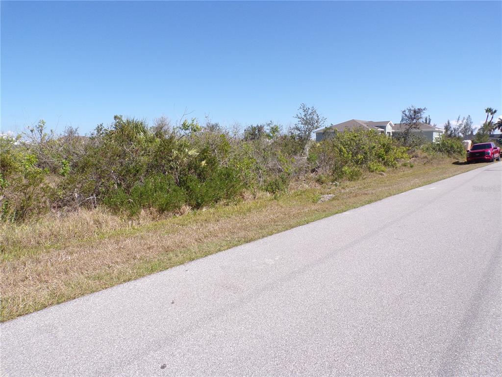 A vacant, overgrown lot sits beside a paved road with a red truck parked nearby — 15547 MCCOMB CIRCLE, PORT CHARLOTTE, FL