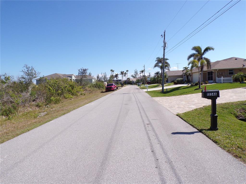 A paved residential street features a mailbox in the foreground and houses with palm trees — 15547 MCCOMB CIRCLE, PORT CHARLOTTE, FL