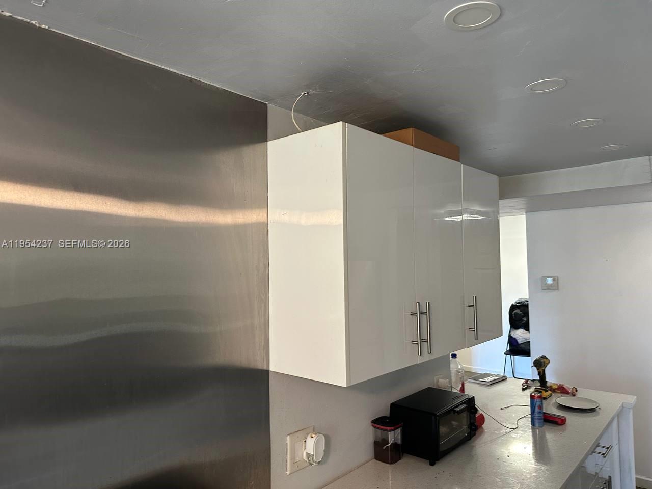 A kitchen features white upper cabinets, a stainless steel backsplash, and a countertop with appliances — 3720 Inverrary Dr # 1L, Lauderhill FL 33319, LAUDERHILL, FL