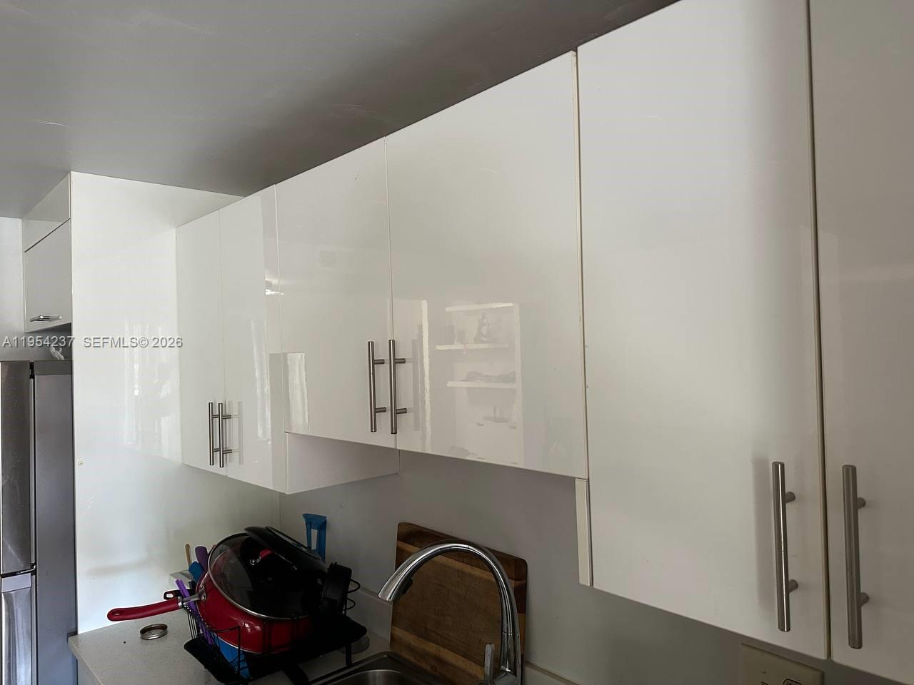 White high-gloss kitchen cabinets are mounted above a stainless steel sink and faucet — 3720 Inverrary Dr # 1L, Lauderhill FL 33319, LAUDERHILL, FL