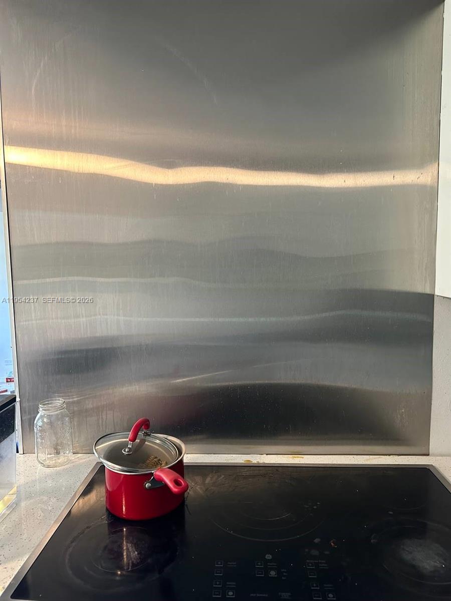 A stainless steel backsplash sits behind a black glass cooktop with a red pot — 3720 Inverrary Dr # 1L, Lauderhill FL 33319, LAUDERHILL, FL