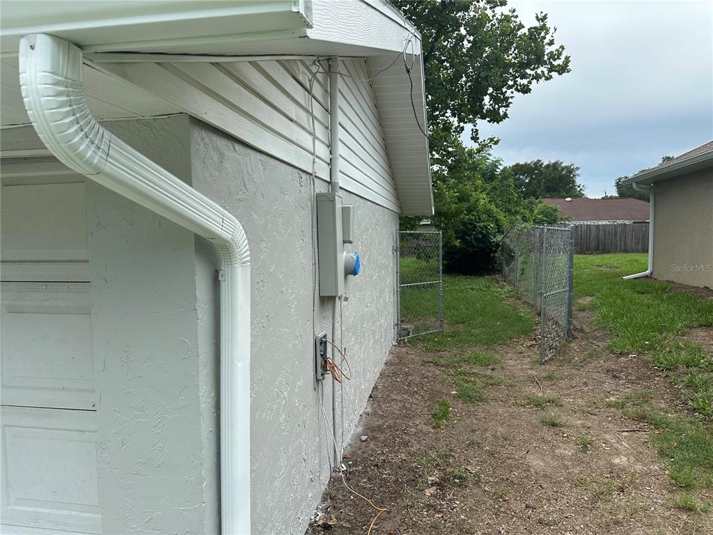 The exterior side of a house features a white gutter, stucco wall, and electrical equipment — 13678 SE 55TH AVENUE, SUMMERFIELD, FL