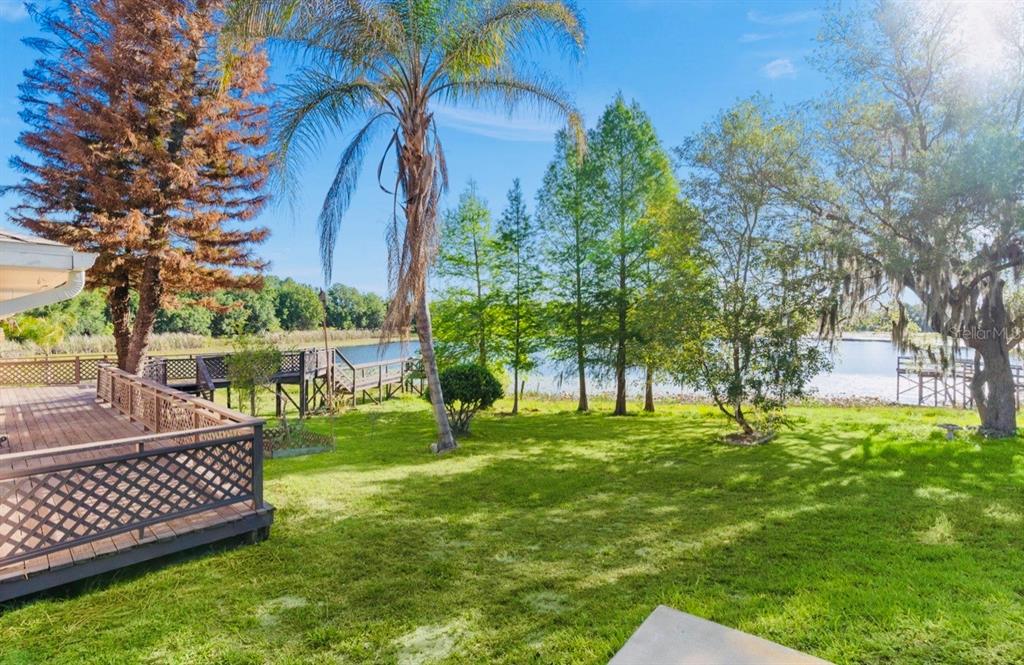 A wooden deck overlooks a grassy backyard with trees and a lake in the distance — 9440 COUNTY ROAD 561, CLERMONT, FL