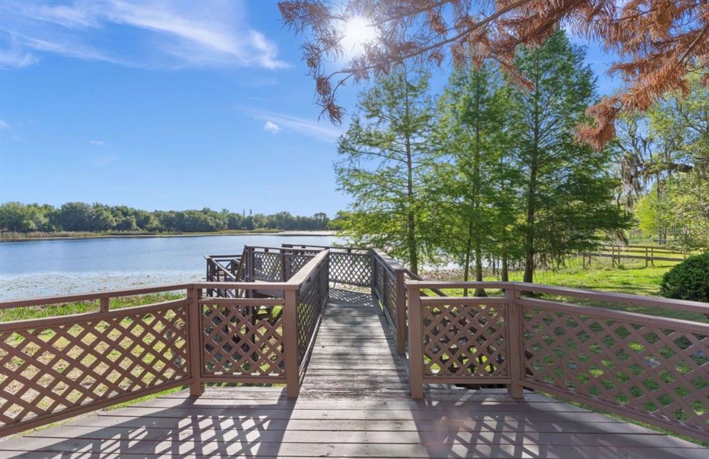 A wooden deck with lattice railings overlooks a lake surrounded by trees under a sunny sky — 9440 COUNTY ROAD 561, CLERMONT, FL