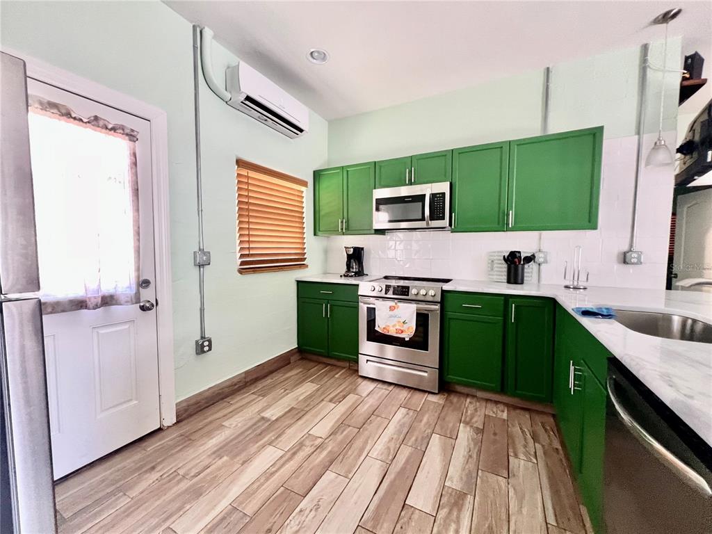A kitchen features green cabinets, stainless steel appliances, white countertops, and wood-look tile flooring — 821 MULBERRY STREET UNIT D, MAITLAND, FL