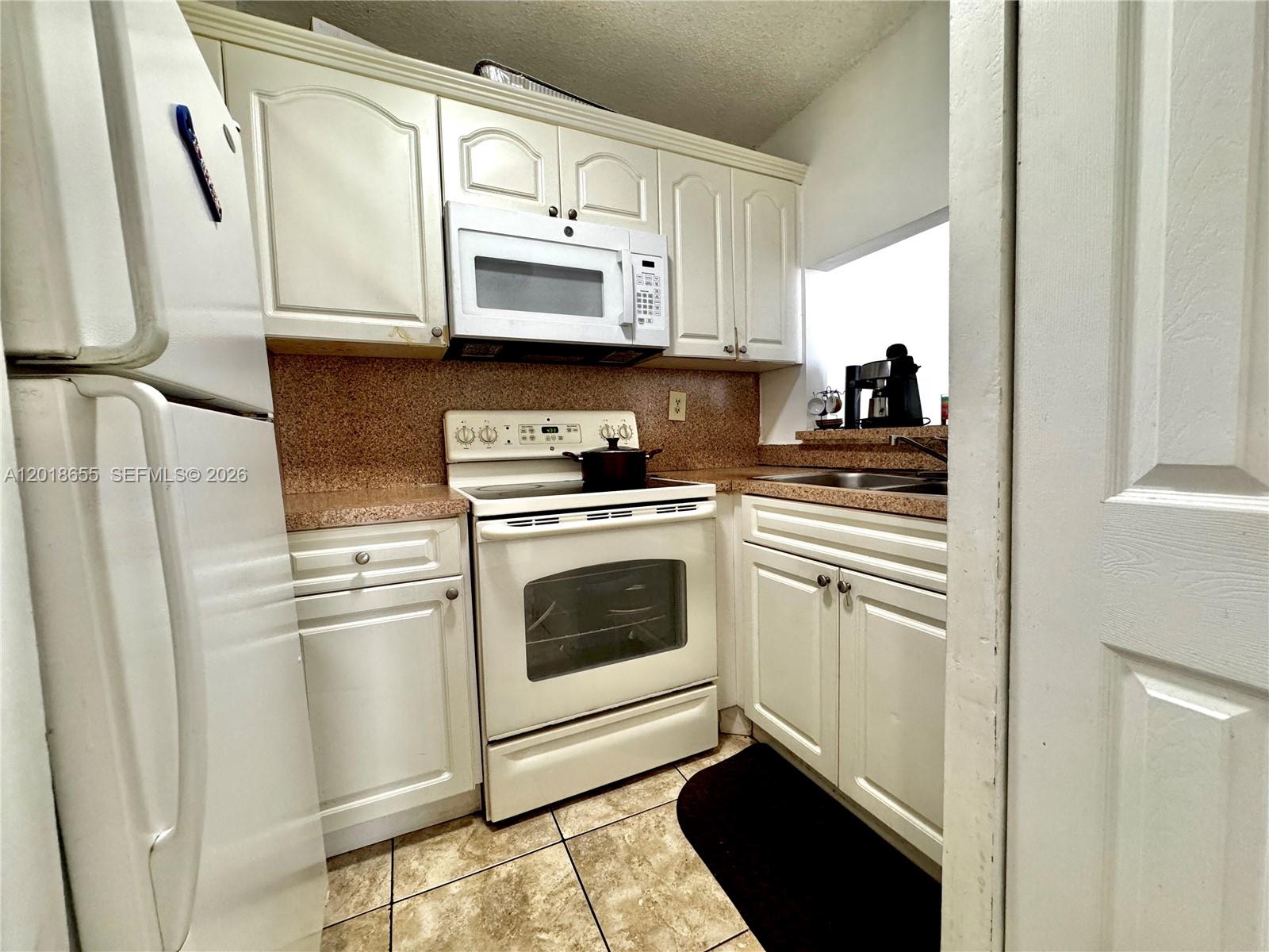 A small kitchen features white cabinets, a white stove, a microwave, and tan countertops — 8145 NW 7th St # 404, Miami FL 33126, MIAMI, FL