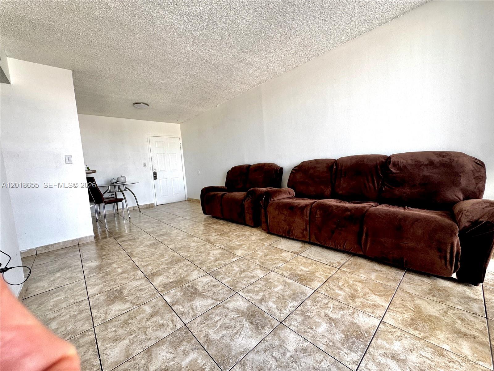 A living room features brown reclining sofas, tile flooring, and a small dining table — 8145 NW 7th St # 404, Miami FL 33126, MIAMI, FL