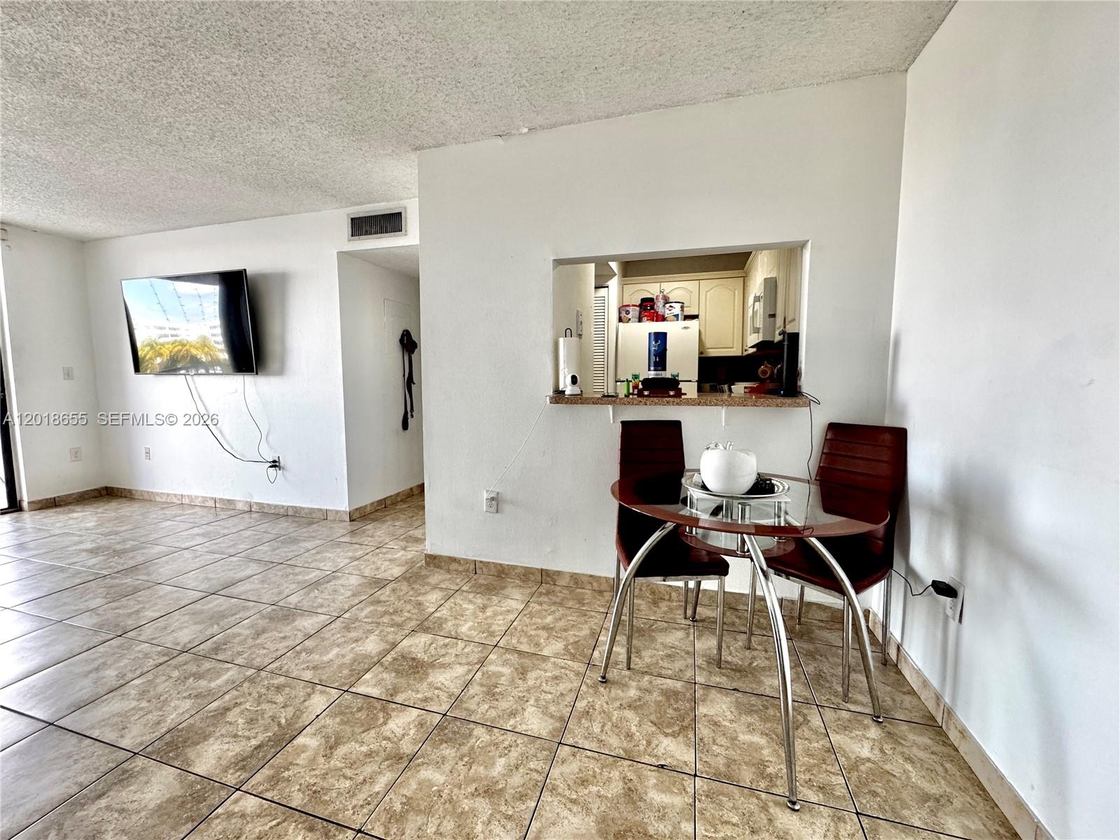 A dining area with a glass table and chairs sits before a kitchen pass-through window — 8145 NW 7th St # 404, Miami FL 33126, MIAMI, FL