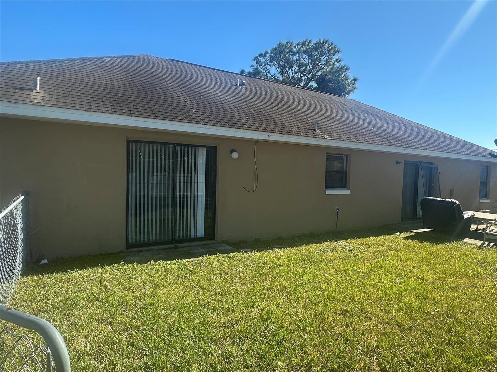 The exterior of a tan house features a shingled roof, sliding glass doors, and windows — 813 Seven Gables Circle, Palm Bay FL 32909, PALM BAY, FL