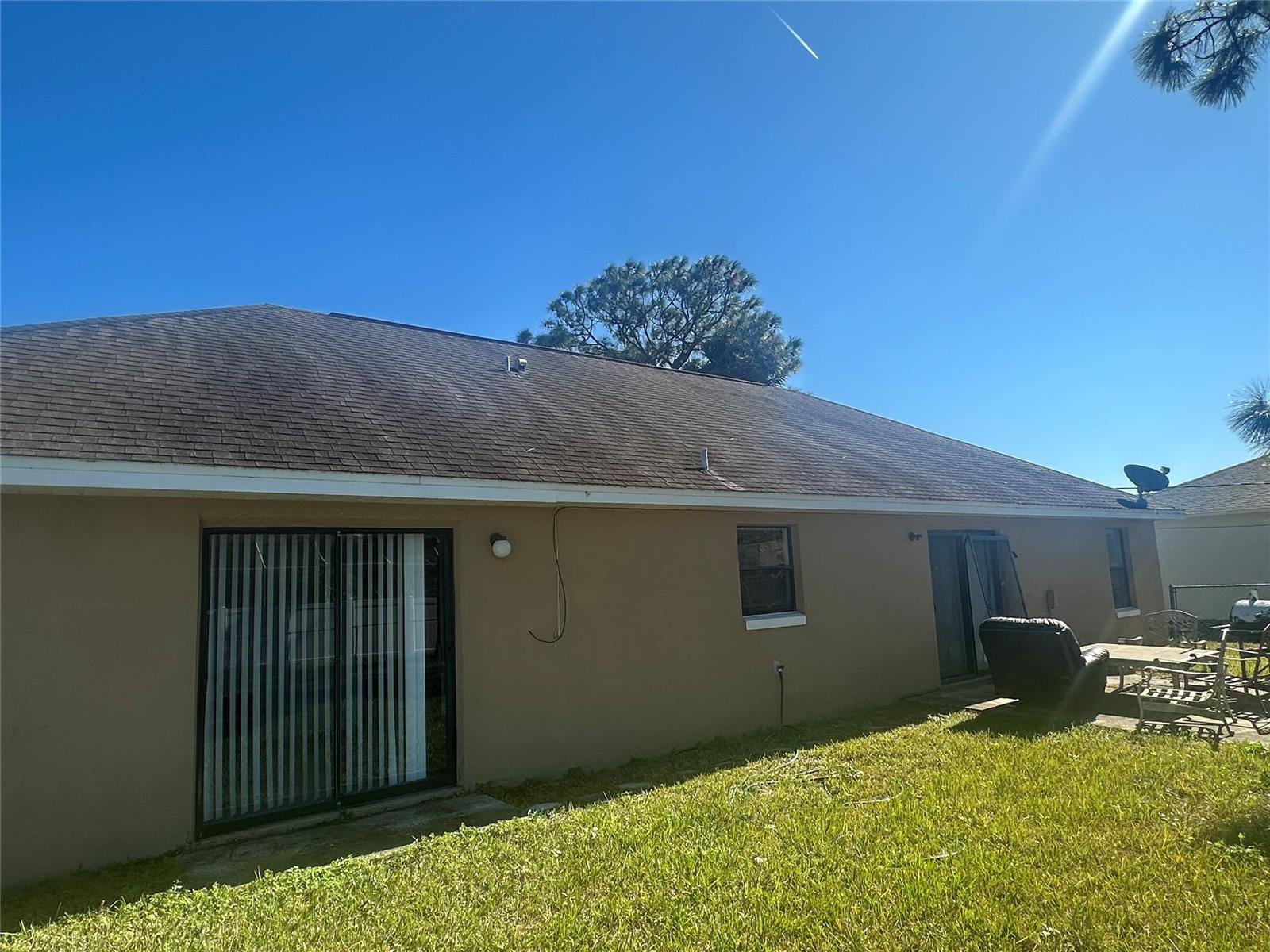 The exterior of a tan house features a shingled roof, sliding glass doors, and windows — 813 Seven Gables Circle, Palm Bay FL 32909, PALM BAY, FL
