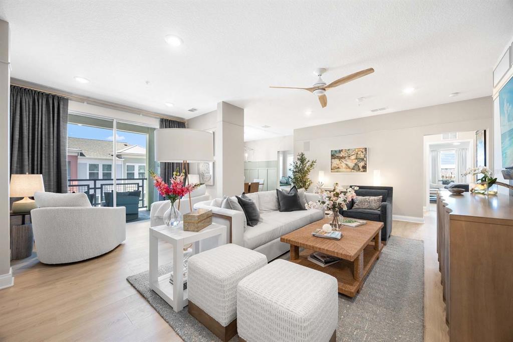 A bright living room features a white sofa, two ottomans, a coffee table, and balcony access — 7557 LAUREATE BOULEVARD UNIT 6407, ORLANDO, FL