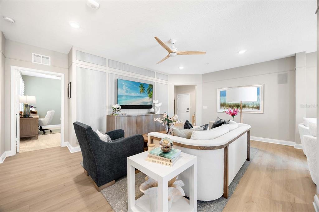 A living room features a white sofa, a dark armchair, and a wall-mounted television — 7557 LAUREATE BOULEVARD UNIT 6407, ORLANDO, FL