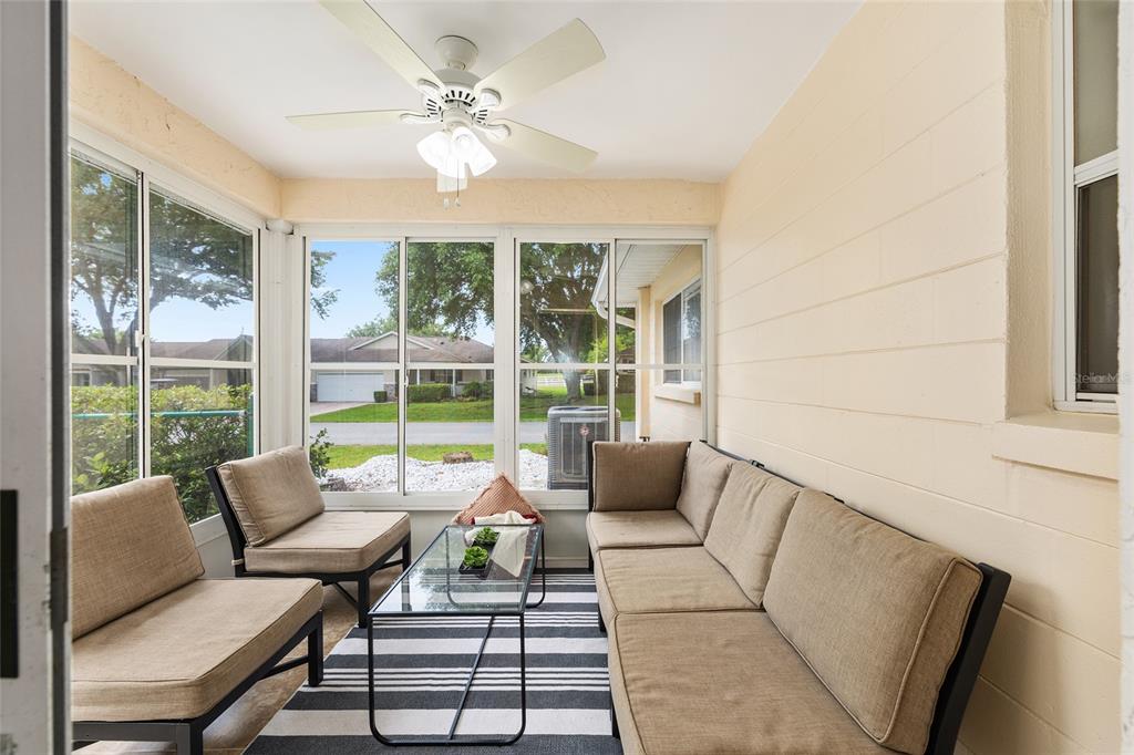 A sunroom features a ceiling fan, a glass-topped coffee table, and outdoor furniture on a rug — 9755 SW 94TH TERRACE UNIT D, OCALA, FL