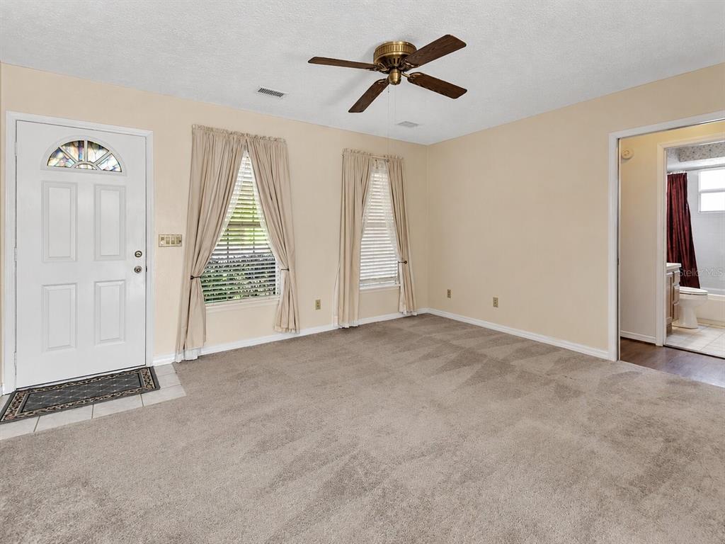 A carpeted living room features a ceiling fan, two windows with curtains, and a doorway — 1141 8TH AVENUE, DELAND, FL