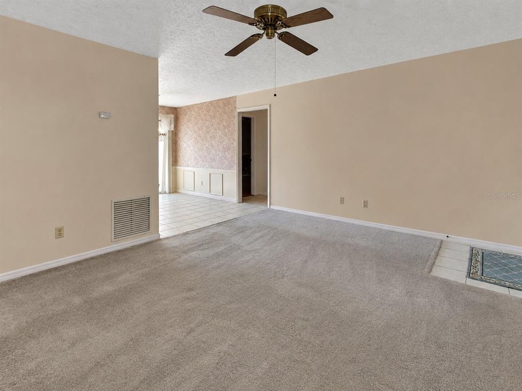 A carpeted living room transitions into a tiled dining area with wainscoting and a ceiling fan — 1141 8TH AVENUE, DELAND, FL