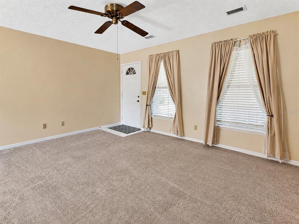 A carpeted living room features a ceiling fan, a white front door, and two windows — 1141 8TH AVENUE, DELAND, FL